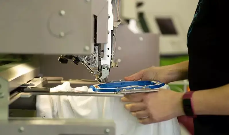 Nahaufnahme einer Stickmaschine auf der gerade ein Kleidungsstück eingespannt wird.